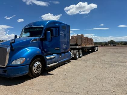 Kenworth day cab with a loaded flatbed behind it