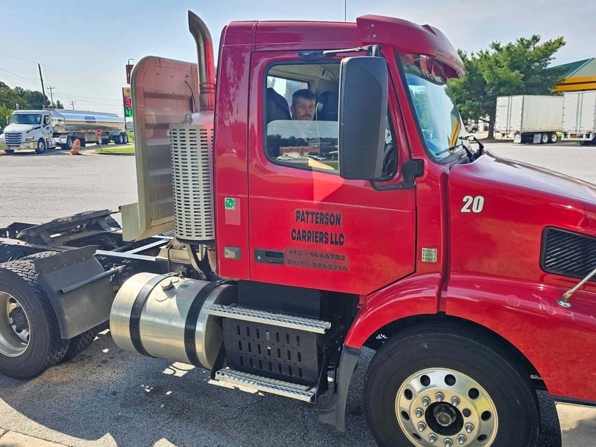 A driver in the cab of a red day cab tractor
